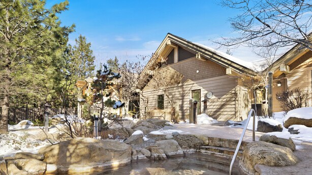 Un chalet doté d’un bain à remous en pierre, d’une façade en bois et offrant une vue sur un ciel dégagé.