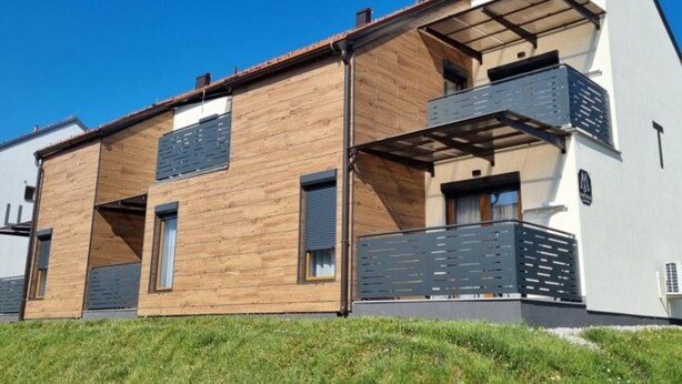 A modern two-story house with a wooden facade, a balcony on the upper floor, and a visible garage door.