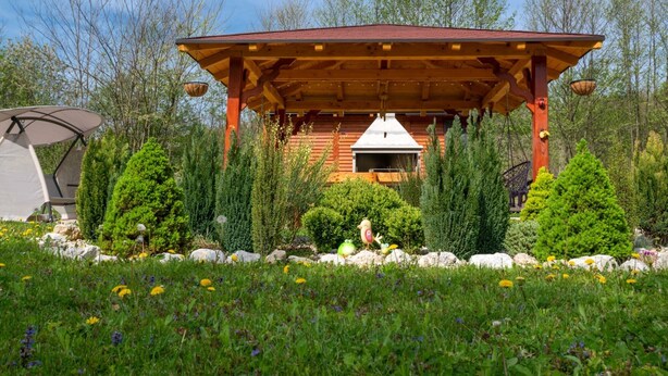 A wooden cabin with a covered patio, surrounded by lush greenery and trees.