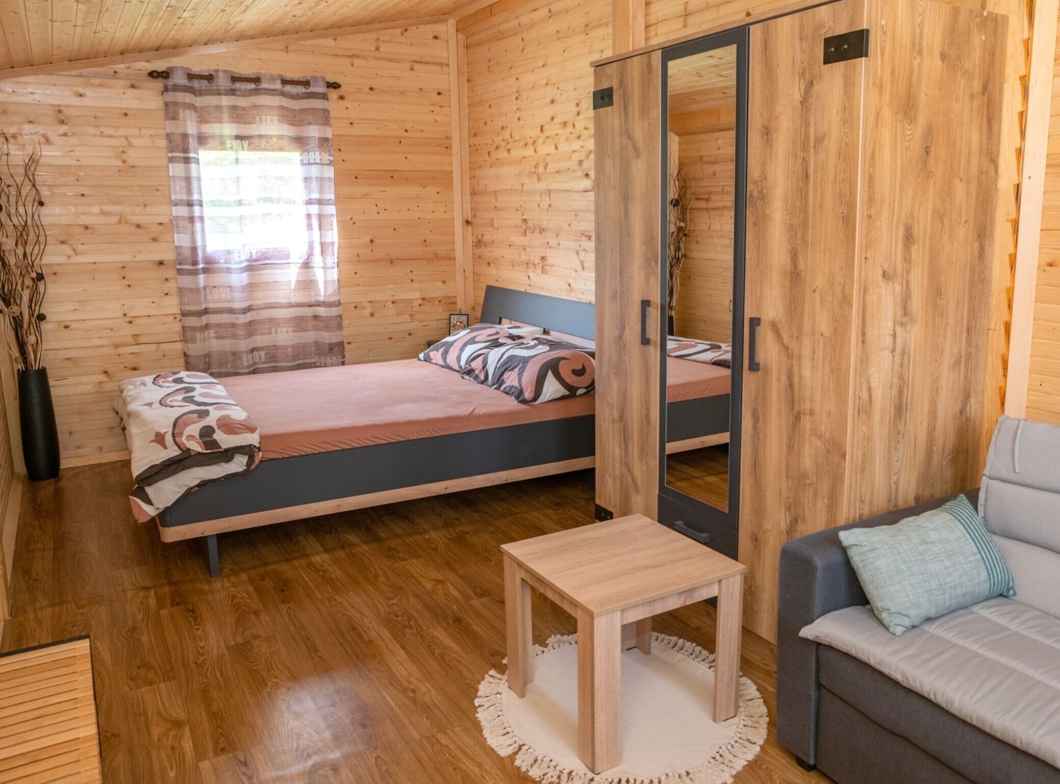 A wooden cabin room with two beds, a sofa, a small table, and a mirror.