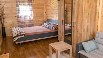 A wooden cabin room with two beds, a sofa, a small table, and a mirror.