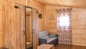 A cozy room with wooden walls, a sofa, a small table, and a window with curtains.