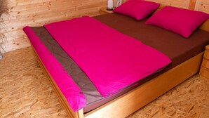 Una cama de madera con un edredón y almohadas de color rosa brillante, un cabecero de madera y una mesita de noche con una lámpara.