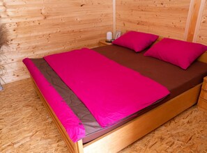 Una cama de madera con un edredón y almohadas de color rosa brillante, un cabecero de madera y una mesita de noche con una lámpara.