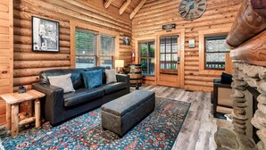A log cabin interior with a leather sofa, a patterned rug, wooden walls, and a clock. - Mountain Retreat in the Smoky Mountain Near Dollywood (Pigeon Forge)