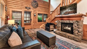A log cabin interior with a stone fireplace, a leather sofa, and a large window. - Mountain Retreat in the Smoky Mountain Near Dollywood (Pigeon Forge)