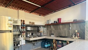 A compact kitchen with a refrigerator, microwave, and gas stove. There are shelves with kitchenware and storage containers. - Zayali Bacalar - Guest House (Bacalar)