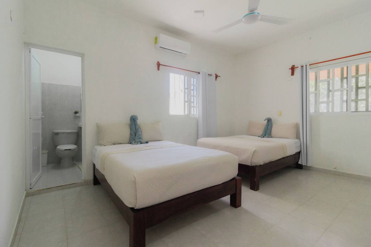 A bedroom with two beds, a ceiling fan, an air conditioning unit, and a window with curtains.