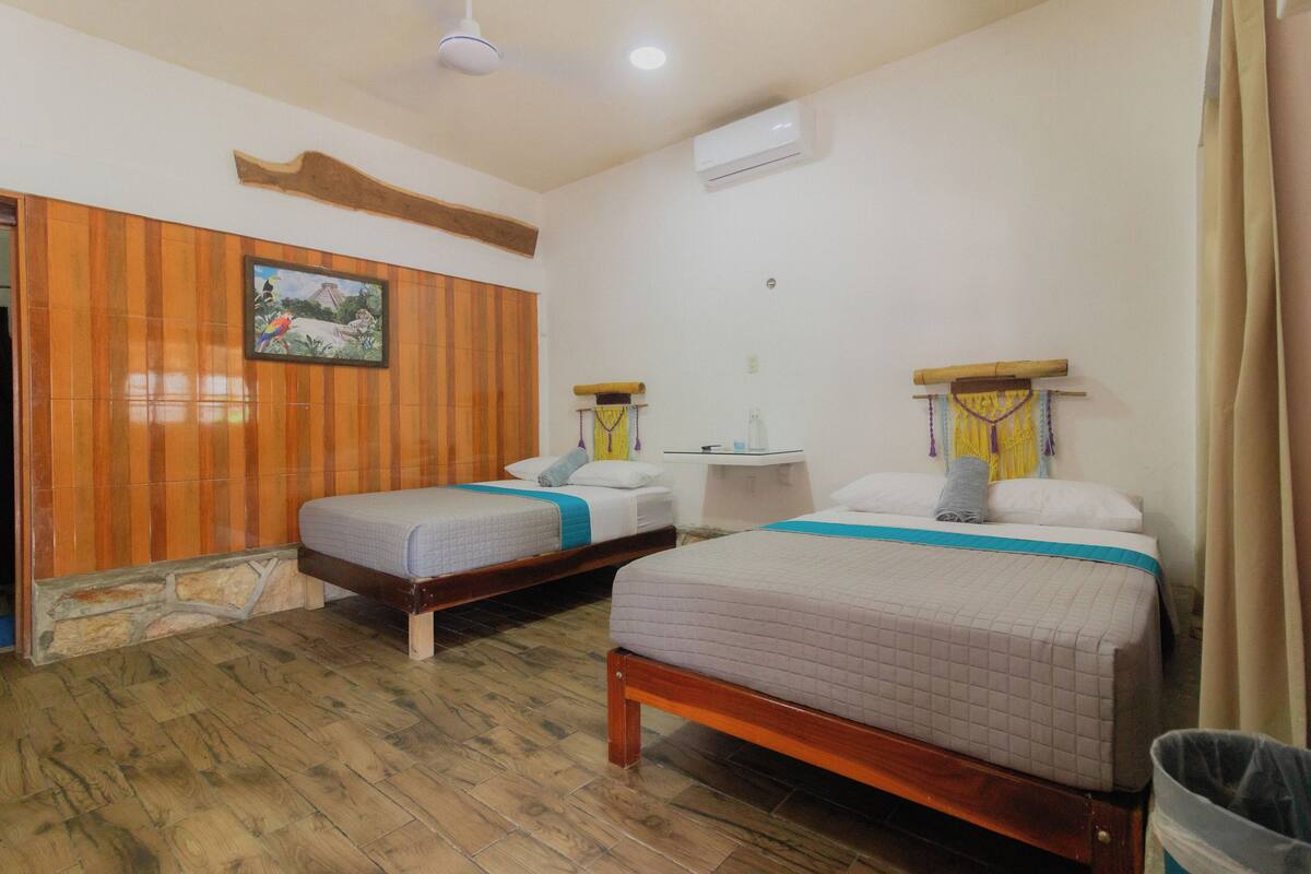 A hotel room with two single beds, wooden paneling on the walls, a small table, and a ceiling fan.