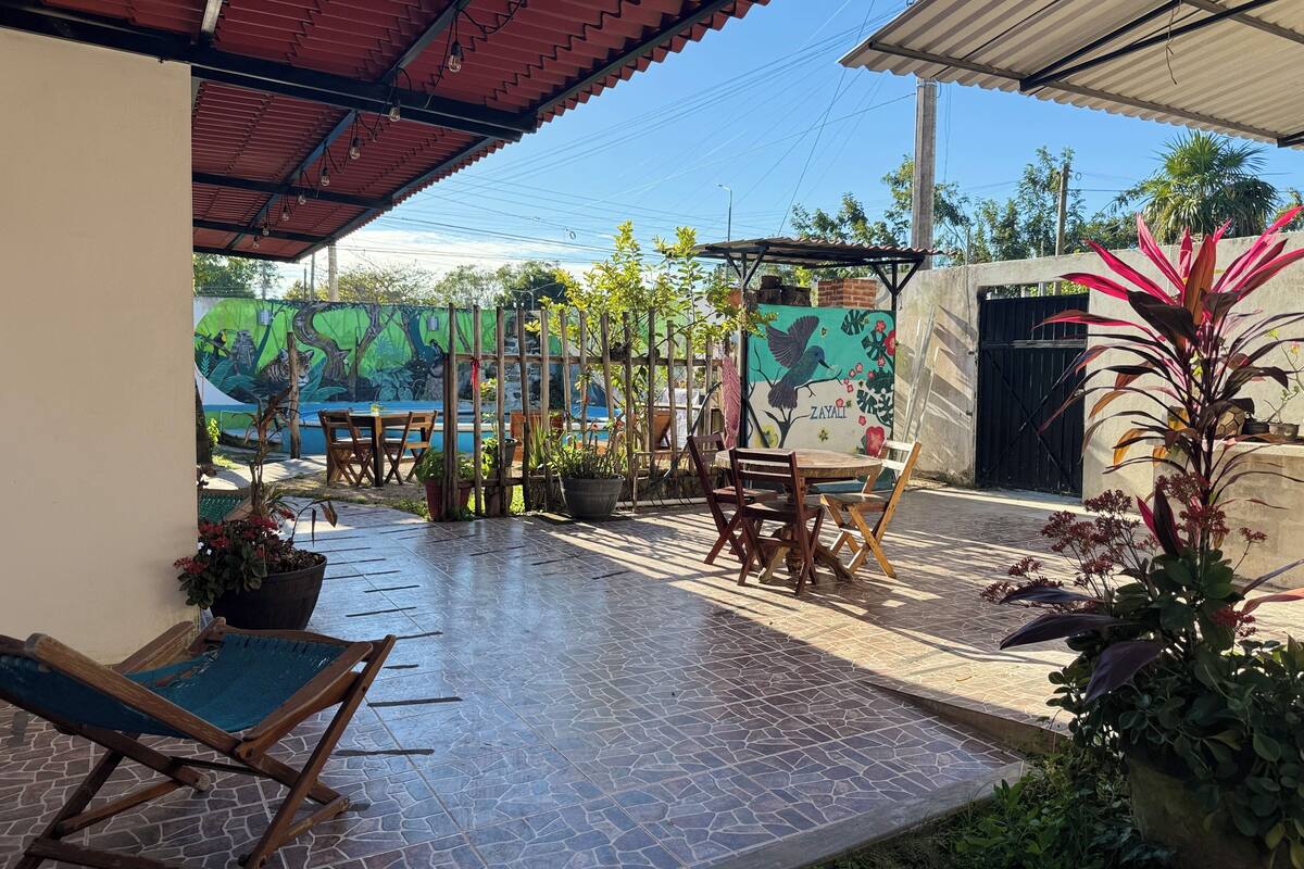 An outdoor patio with tiled flooring, wooden furniture, potted plants, and a mural on the wall.