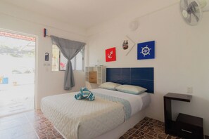 Un dormitorio con cama, mesita de noche, ventilador y decoración en la pared, incluyendo una rueda de barco y un ancla.