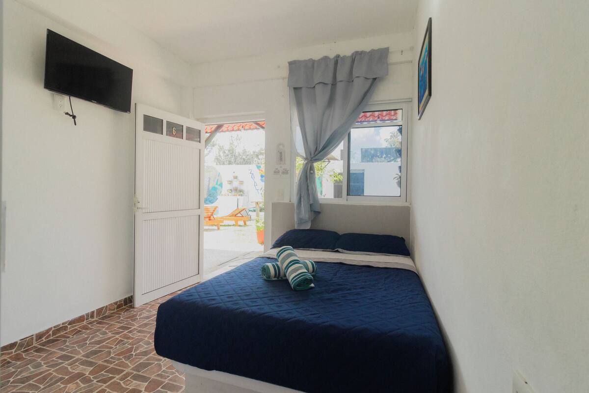 A bedroom with a bed, a window with curtains, a TV mounted on the wall, and a door leading to an outdoor area.