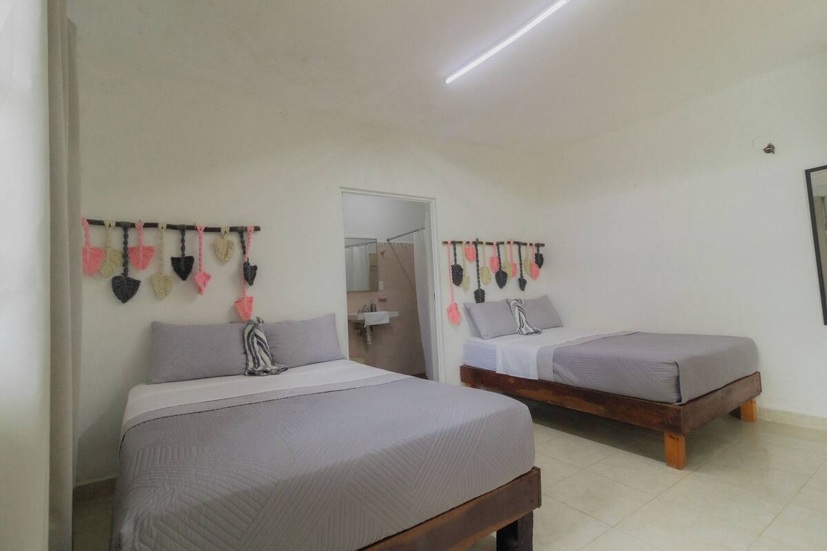 A bedroom with two beds, a wooden headboard, a white wall, and a hanging decoration.