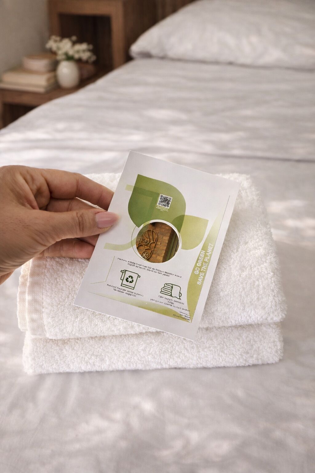 A hand holding a white package with a QR code and text on a white towel on a bed.