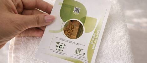 A hand holding a white package with a QR code and text on a white towel on a bed.
