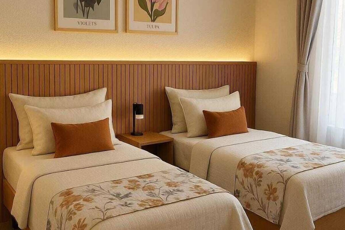 Ein Hotelzimmer mit zwei Betten, Holz-Kopfteilen, einem Nachttisch und gerahmten Pflanzenbildern an der Wand.