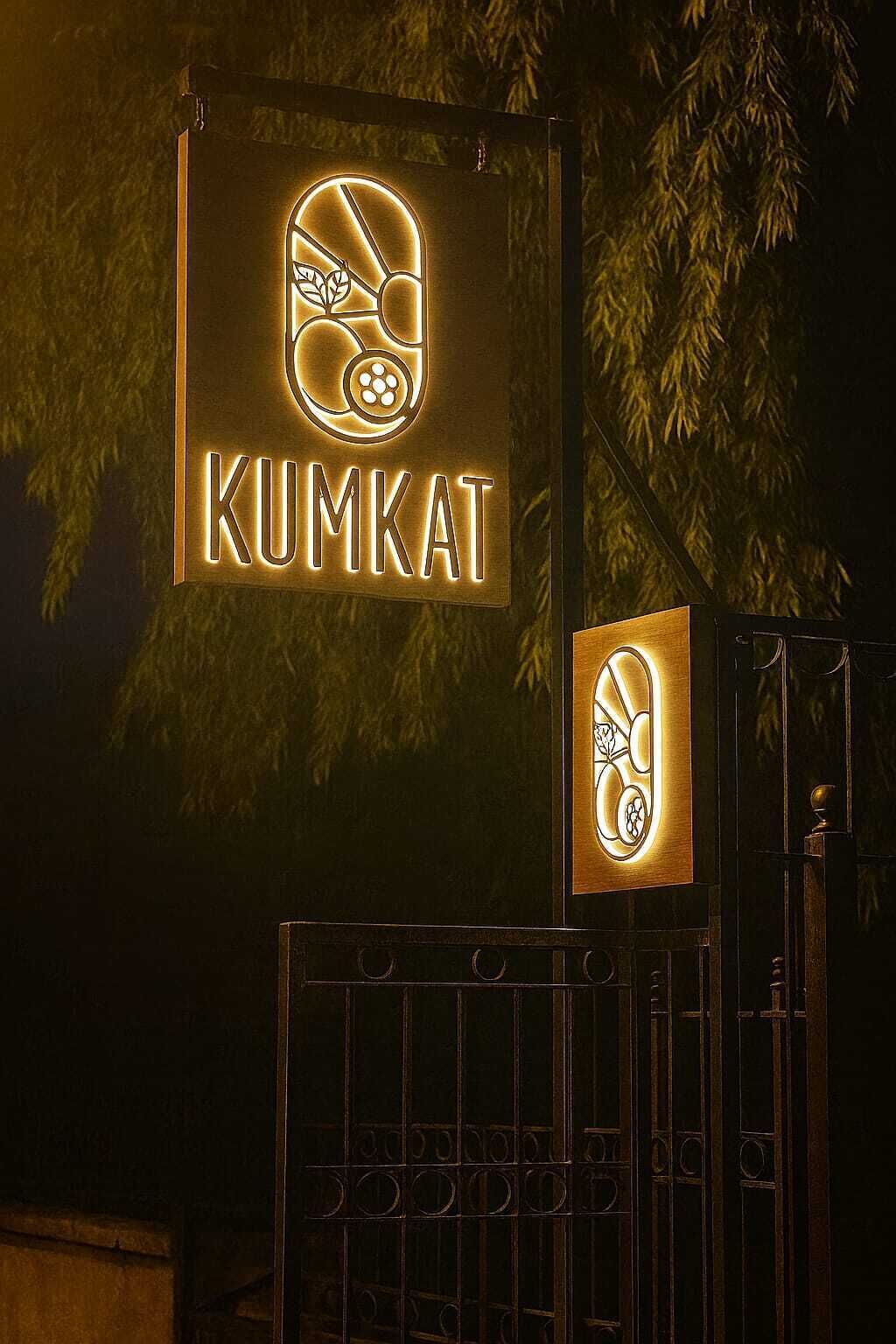 Een bord met de naam 'KUMKAT' in neonverlichting, bevestigd aan een metalen poort.