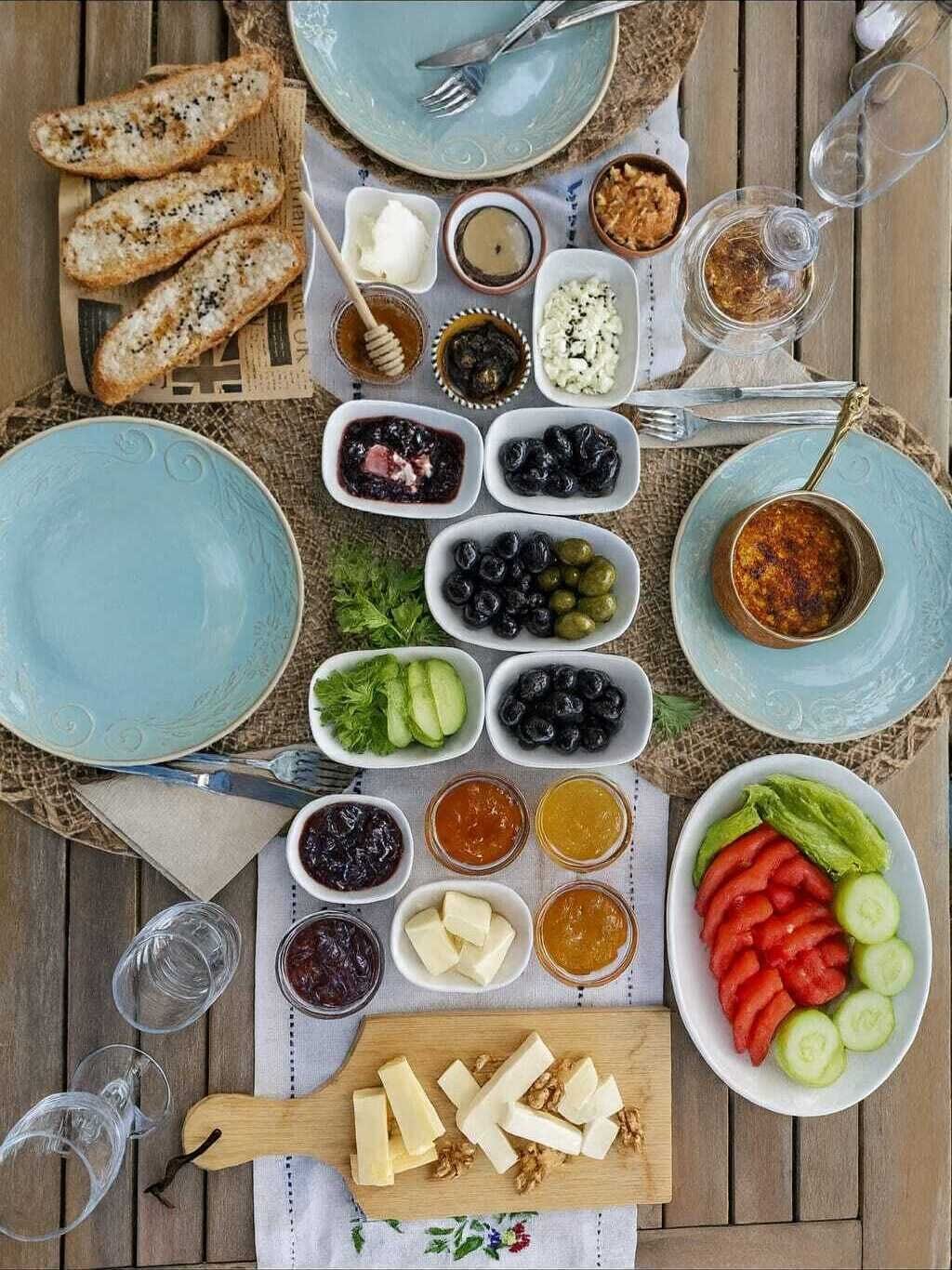 A table set with various food items and utensils, including bread, cheese, olives, and vegetables.