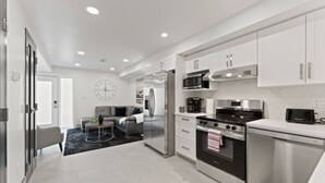 A modern kitchen with stainless steel appliances, white cabinetry, and a grey sofa in the adjacent living area. - Luxury 171-7 Condos with Magnificent Lakeviews (Leamington)
