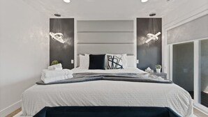 A modern bedroom with a large bed, two pendant lights, a ceiling fan, and a large window. - Luxury 171-11 Condos with Magnificent Lakeviews (Leamington)