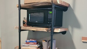 Un estante de madera con un microondas, libros y una cafetera.