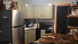 Una cocina con un refrigerador de acero inoxidable, armarios de madera, una estufa negra y una mesa de comedor con mantel marrón.