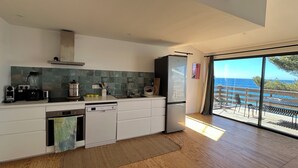 A modern kitchen with a dishwasher, a refrigerator, and a view of the ocean through large windows. - Cabanon Moderne, les Pieds Dans L'eau (Le Pradet)