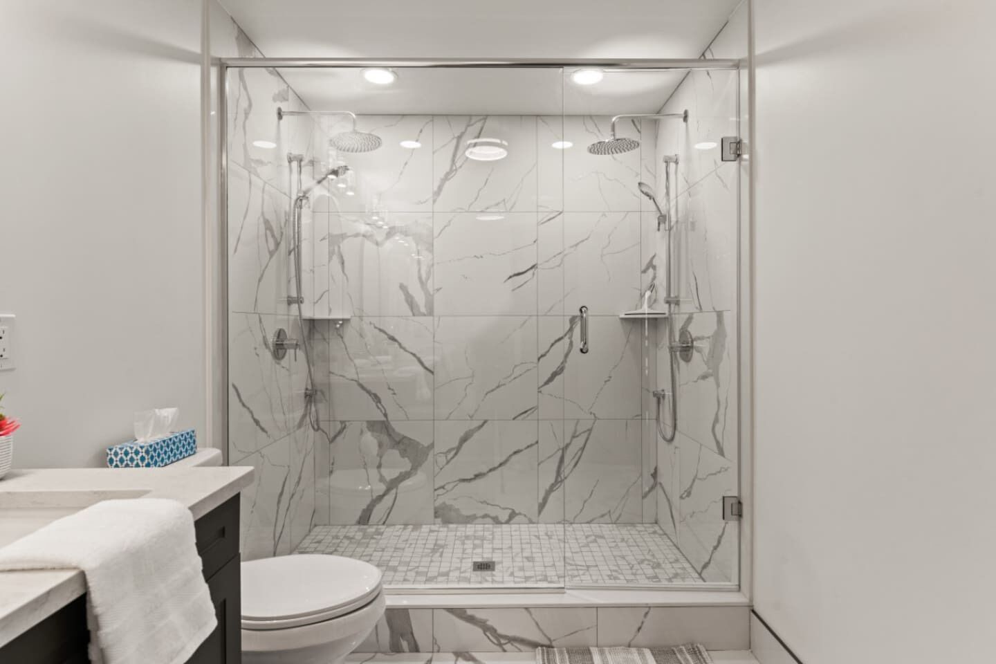 A modern bathroom with a glass-enclosed shower, marble tiles, a toilet, and a sink with a towel.