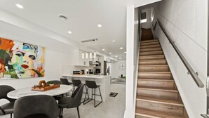 Une cuisine moderne avec des meubles blancs, un coin repas doté d’une table ronde et de chaises, et un escalier en bois.