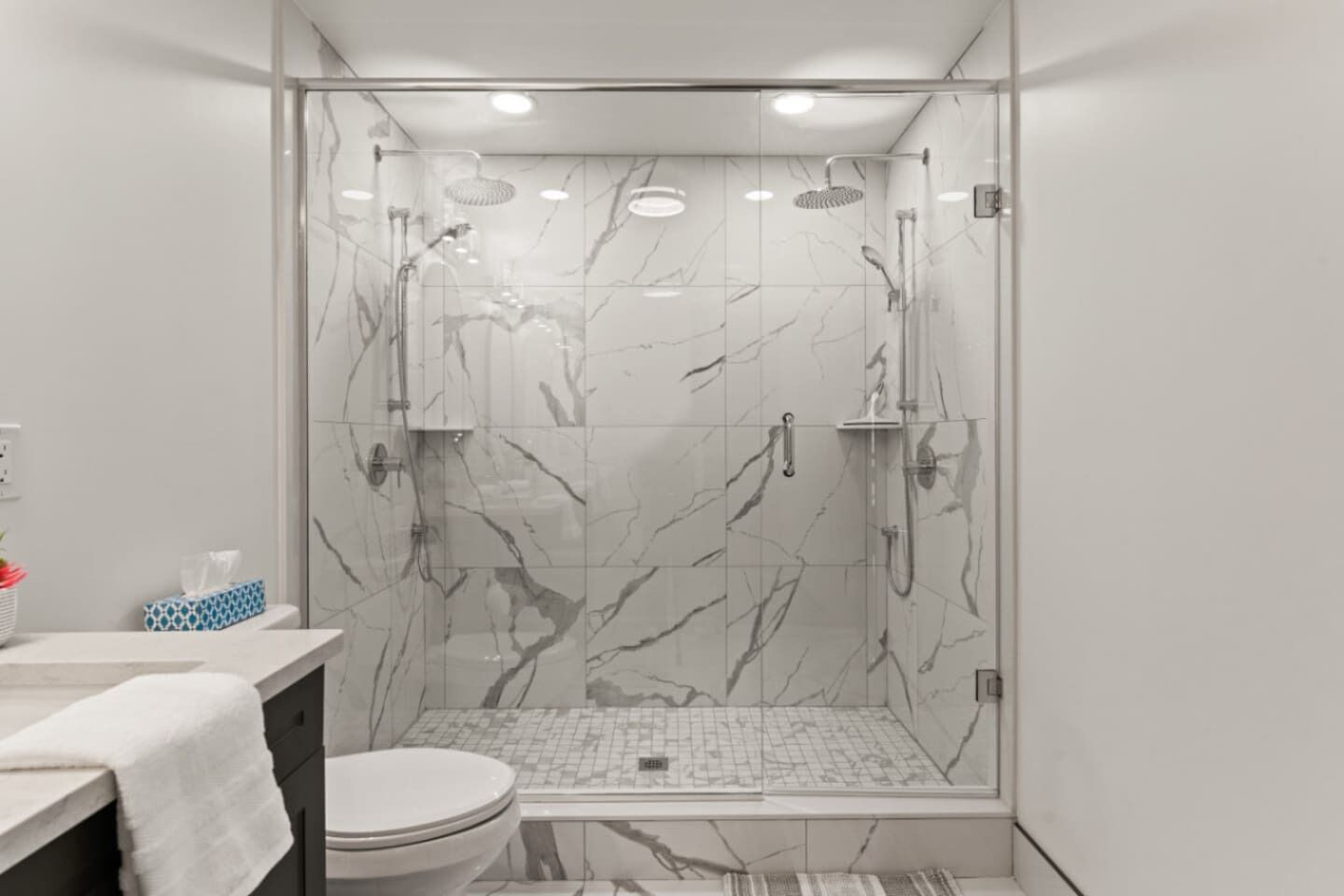 Une salle de bain moderne avec une douche à parois de verre, des carreaux de marbre, des toilettes et un lavabo avec une serviette.