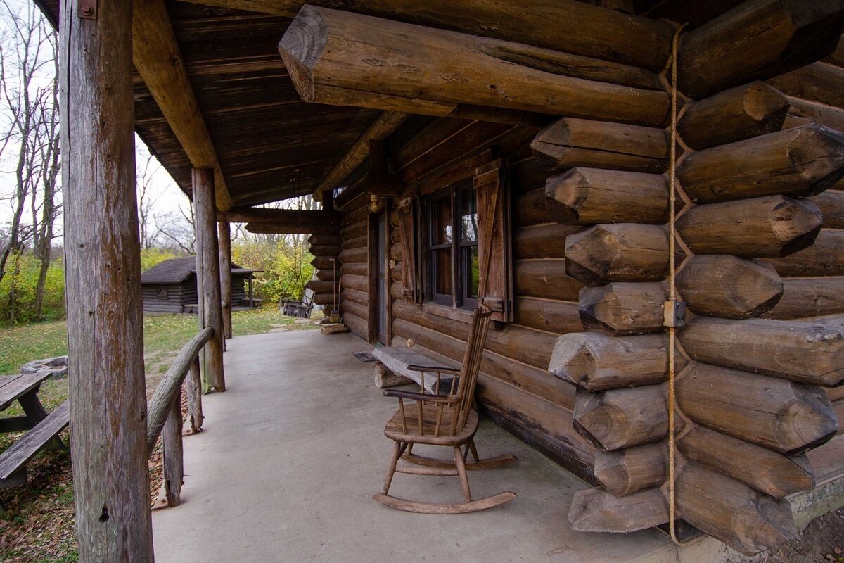 A rustic log cabin with a porch, a rocking chair, and a picnic table.