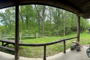 A covered outdoor area with a wooden bench and picnic table, surrounded by trees and a grassy area.