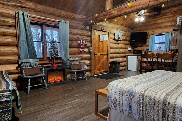 A log cabin interior with a fireplace, wooden furniture, a television, and a bed.