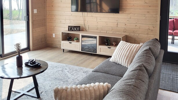 Una sala de estar moderna con un televisor de pantalla plana grande montado en una pared de madera, un sofá gris con almohadones decorativos, una mesita de centro pequeña y un mueble de madera con estantes integrados.