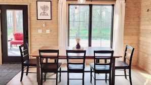 Una habitación con paneles de madera, una mesa de comedor, cuatro sillas, una silla roja afuera y un ventanal con cortinas.