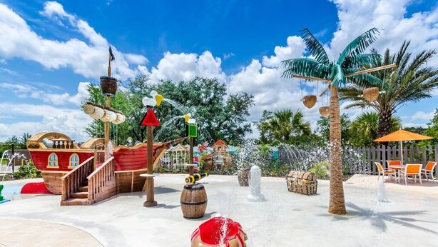 Parque acuático con un barco pirata, palmeras y una zona de arena con una mesa y sillas.