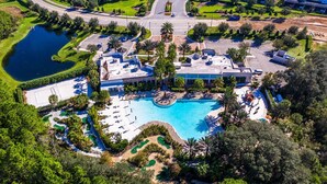 Vista aérea de un complejo turístico con una gran piscina, varios campos de golf y exuberante jardinería.