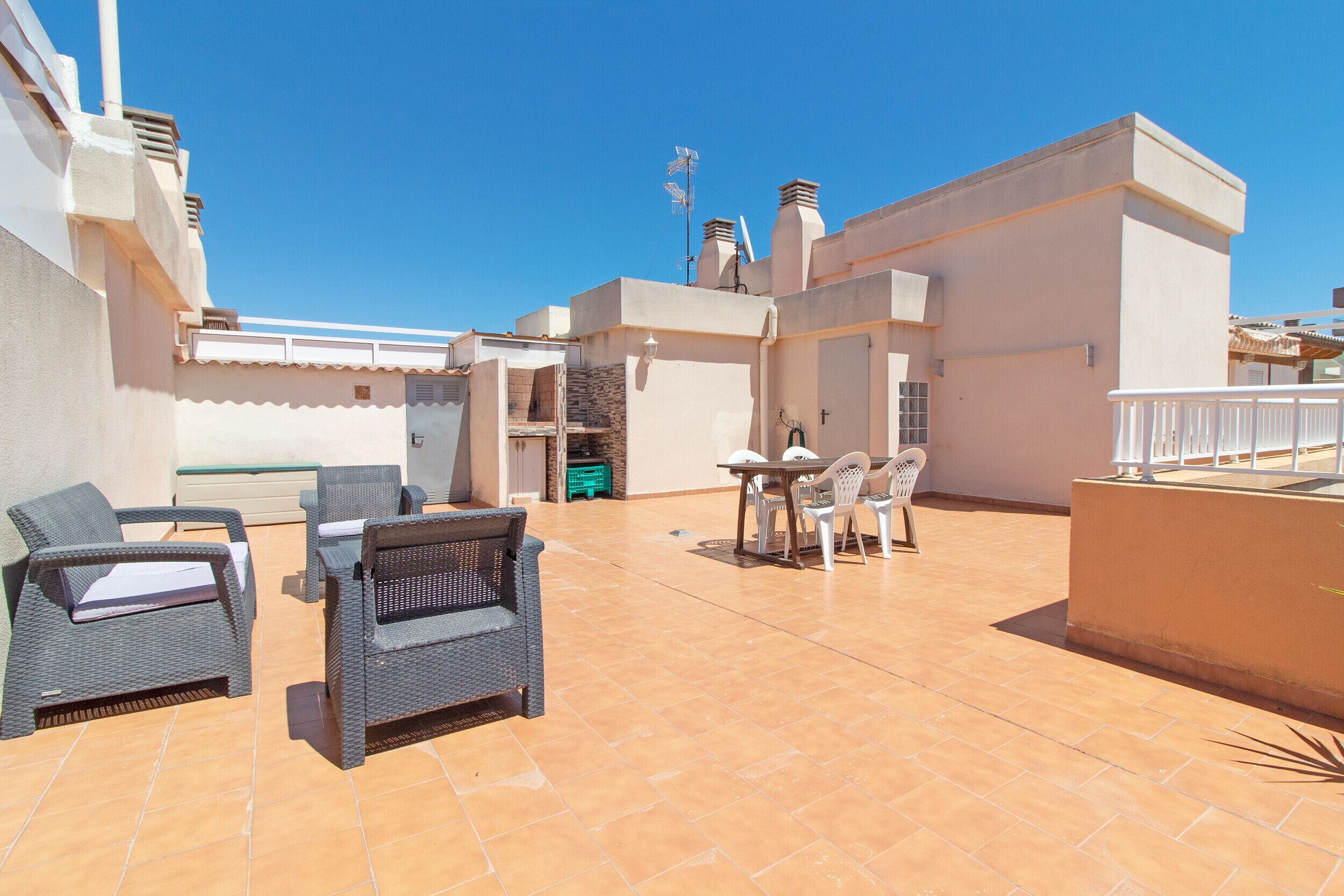 A rooftop patio with wicker furniture, a table, and a view of the sky.
