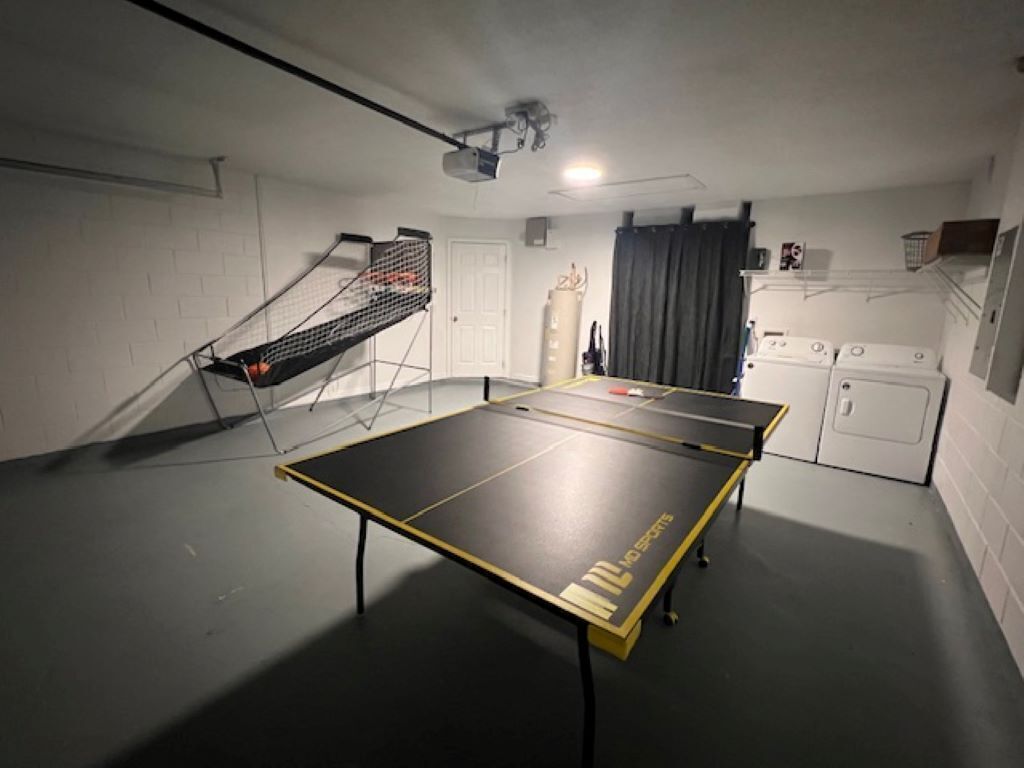 A ping pong table in a room with a laundry area, a door, and a curtain.