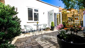 Une cour avec un bâtiment blanc, une porte en verre, une petite table avec des chaises et des plantes en pot.