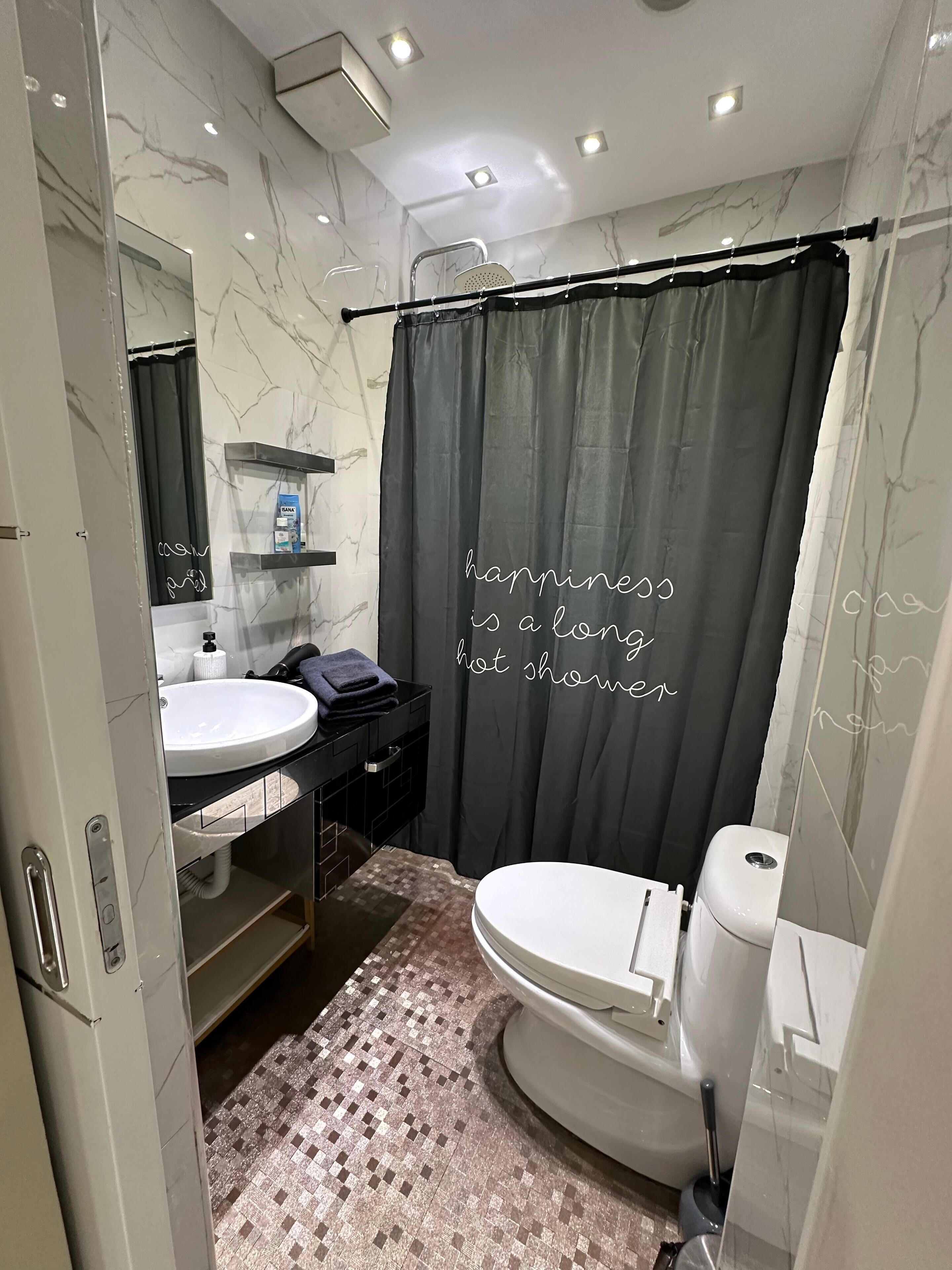 A modern bathroom with a white toilet, a black sink, and a shower curtain with a motivational quote.