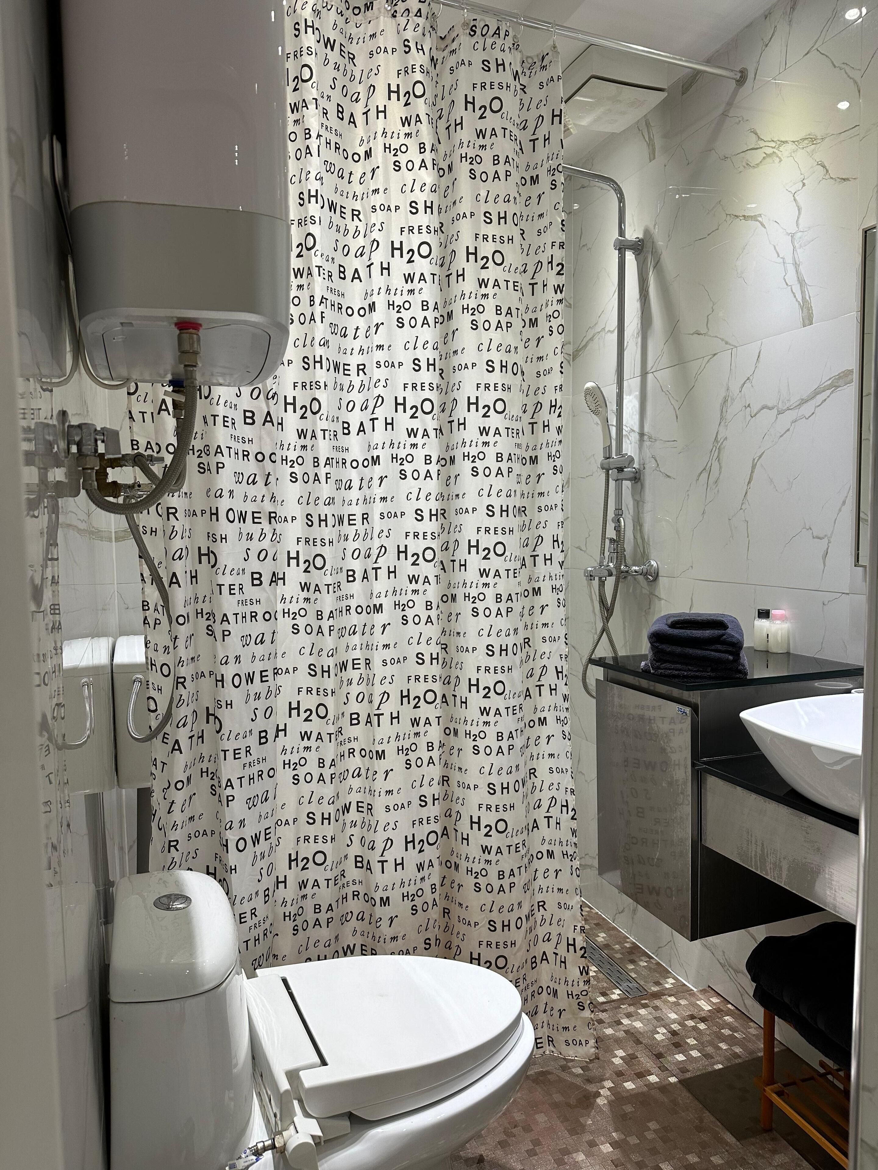 A modern bathroom with a shower curtain, a toilet, a sink, and a handheld showerhead.