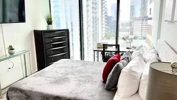 Een moderne slaapkamer met een groot bed, een bureau en uitzicht op hoge gebouwen.