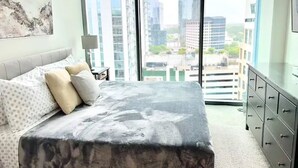 Una camera da letto moderna con un letto grande, una cassettiera e vista sulla città attraverso ampie finestre.