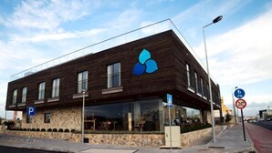 A modern building with a wooden facade, a blue logo, and a pedestrian crossing. - Surfers Lodge Peniche (Peniche)