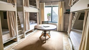 Una habitación pequeña con literas, una mesa redonda y una ventana con cortinas.