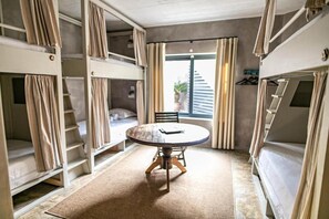 A compact room with bunk beds, a round table, and a window with curtains. - Surfers Lodge Peniche (Peniche)