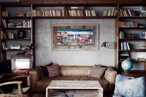 A cozy living room with a brown leather sofa, a coffee table, and a bookshelf filled with books and a globe. - Surfers Lodge Peniche (Peniche)