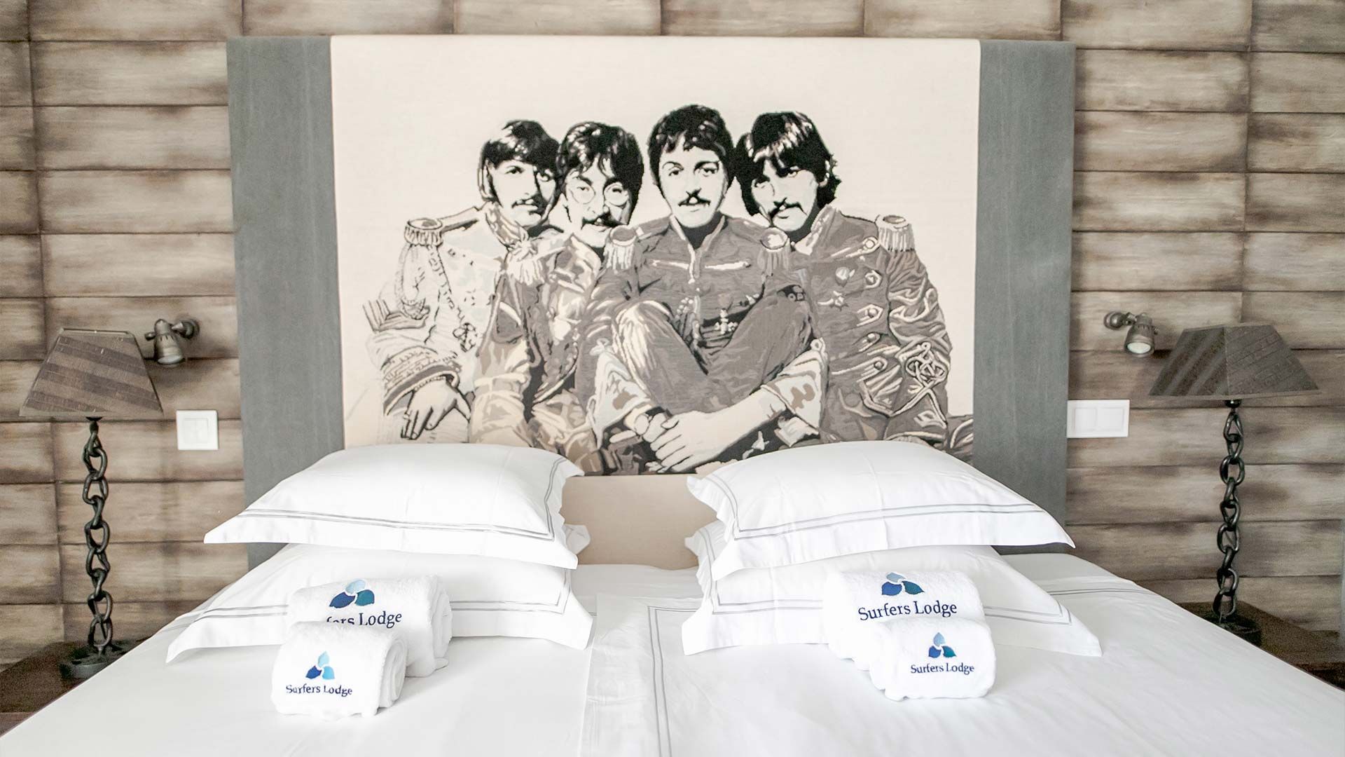 Un lit avec une literie blanche et deux oreillers, chacun portant l’inscription « Surfers Lodge ».