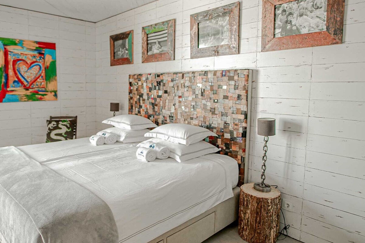 A bedroom with a bed, pillows, a bedside lamp, and a wall art piece.
